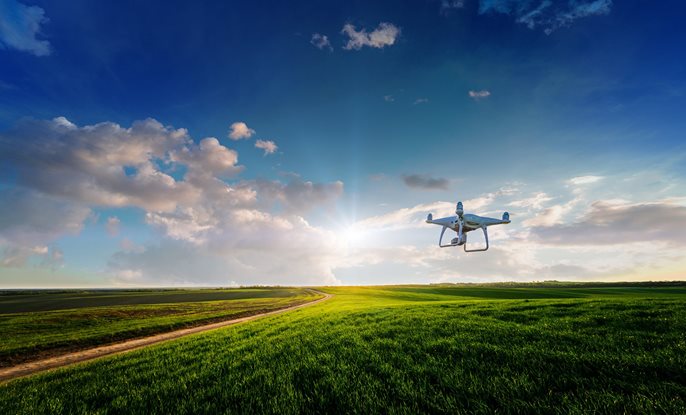 Drone flying through blue sky and over a field.